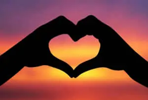 two hands making a heart shape at sunset