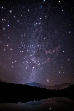 An epic night-time view of a mountain landscape surrounded by a galaxy of stars. 